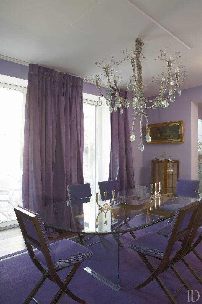 Aménagement d'une salle à manger dans le thème coloré souhaité par la cliente avec table en verre et chaises velours. Ouverture sur la terrasse et vue sur la piscine et le jardin